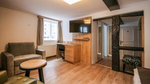 A modern, well-lit room with a sofa, a small round table, a wooden desk, and a TV mounted on the wall. - Zur alten Krone (Hattingen)