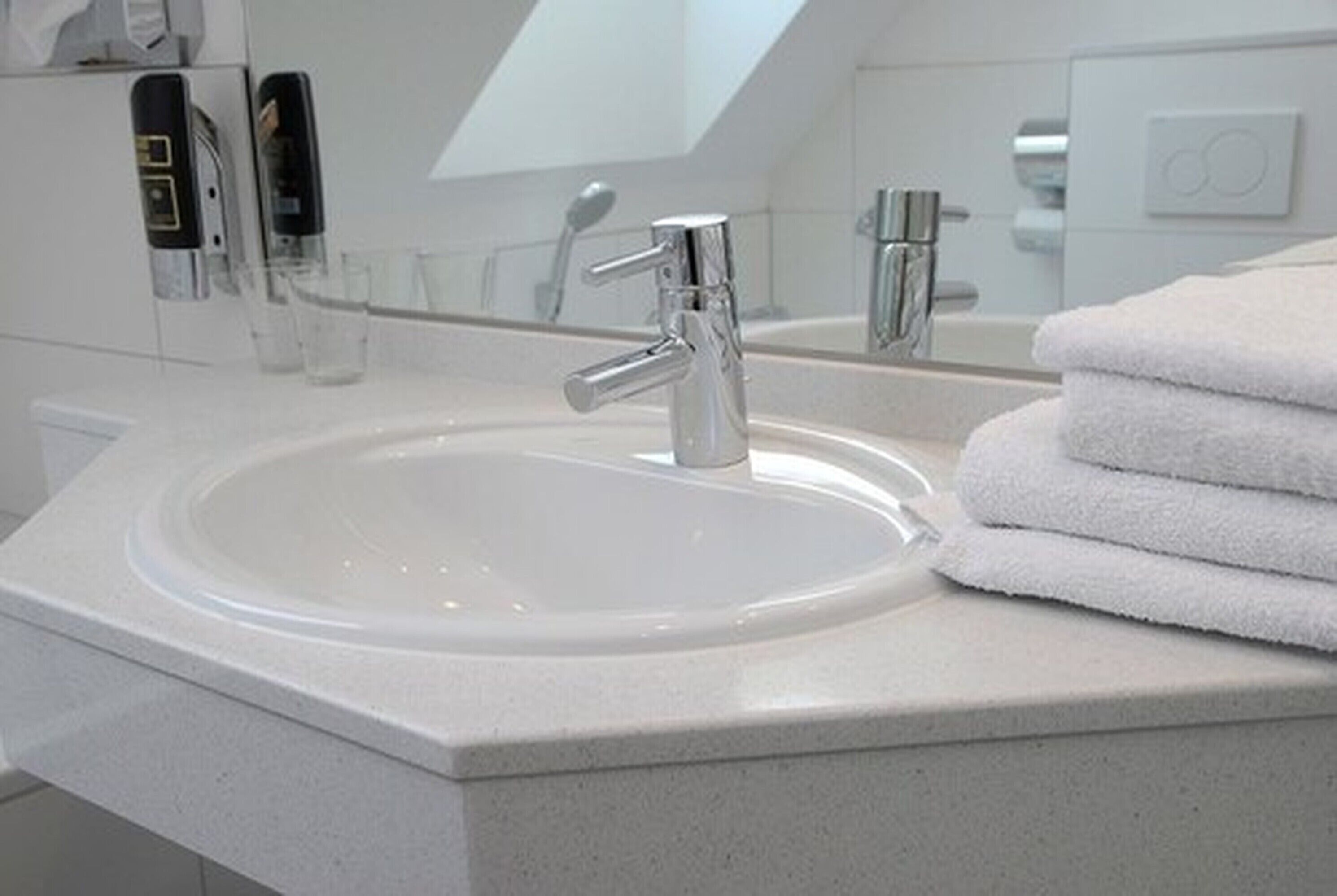 A modern bathroom with a white sink, chrome faucet, and a stack of white towels.