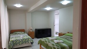A bedroom with two beds, a dresser, a TV, and a door leading to a bathroom.