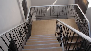 Una escalera con barandilla de metal, escalones color beige y pared blanca.