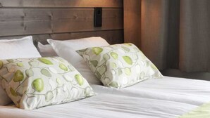Een bed met witte beddengoed en groene kussens, een houten hoofdbord en een wandlamp.