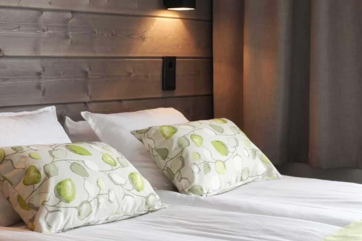 A bed with white bedding and green pillows, a wooden headboard, and a wall-mounted light fixture.