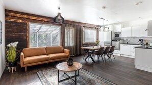 A modern living room with a brown leather sofa, a round coffee table, and a dining area with a wooden table and chairs. - Hotel Metsähirvas (Rovaniemi)