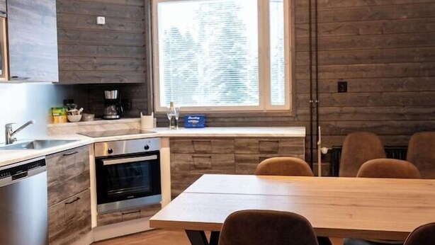 A modern kitchen with wooden cabinetry, a built-in oven, and a dining area with a wooden table and chairs. - Hotel Metsähirvas (Rovaniemi)
