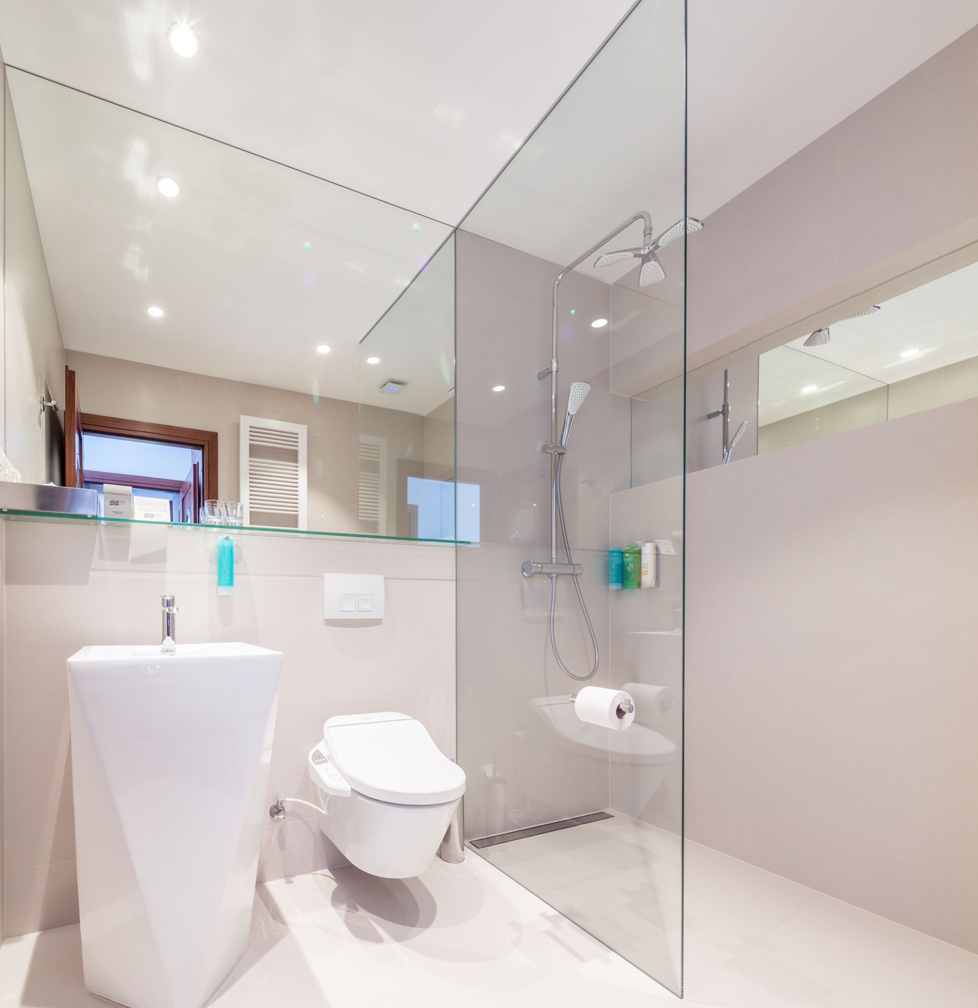 A modern bathroom with a glass-enclosed shower, a white toilet, and a glass shelf above the sink.