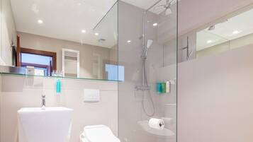Un baño moderno con ducha envuelta en vidrio, inodoro blanco y estante de vidrio sobre el lavabo.