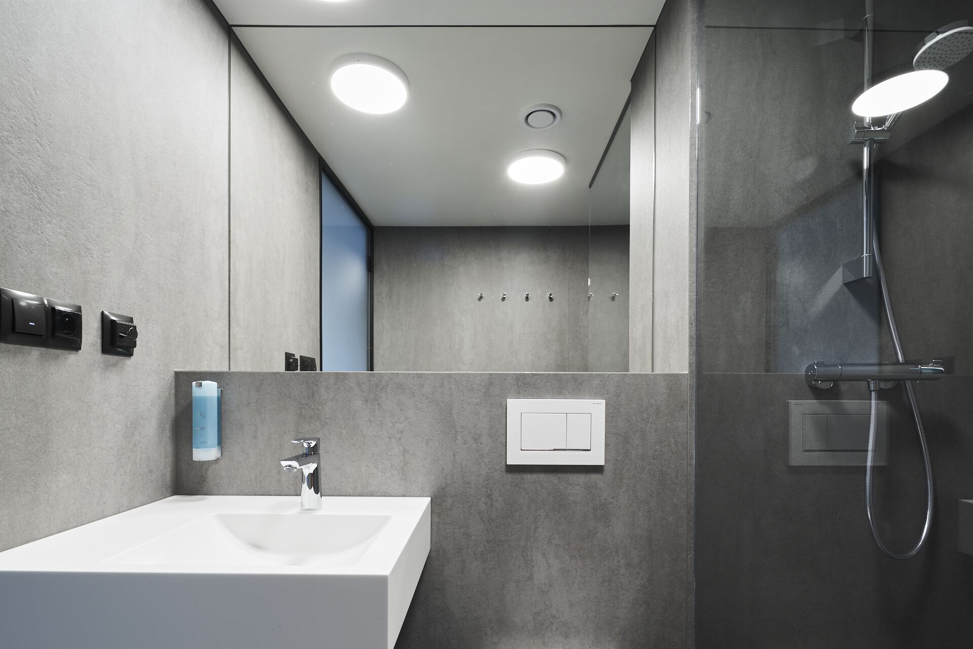 A modern bathroom with a white sink, a handheld showerhead, and a wall-mounted control panel.