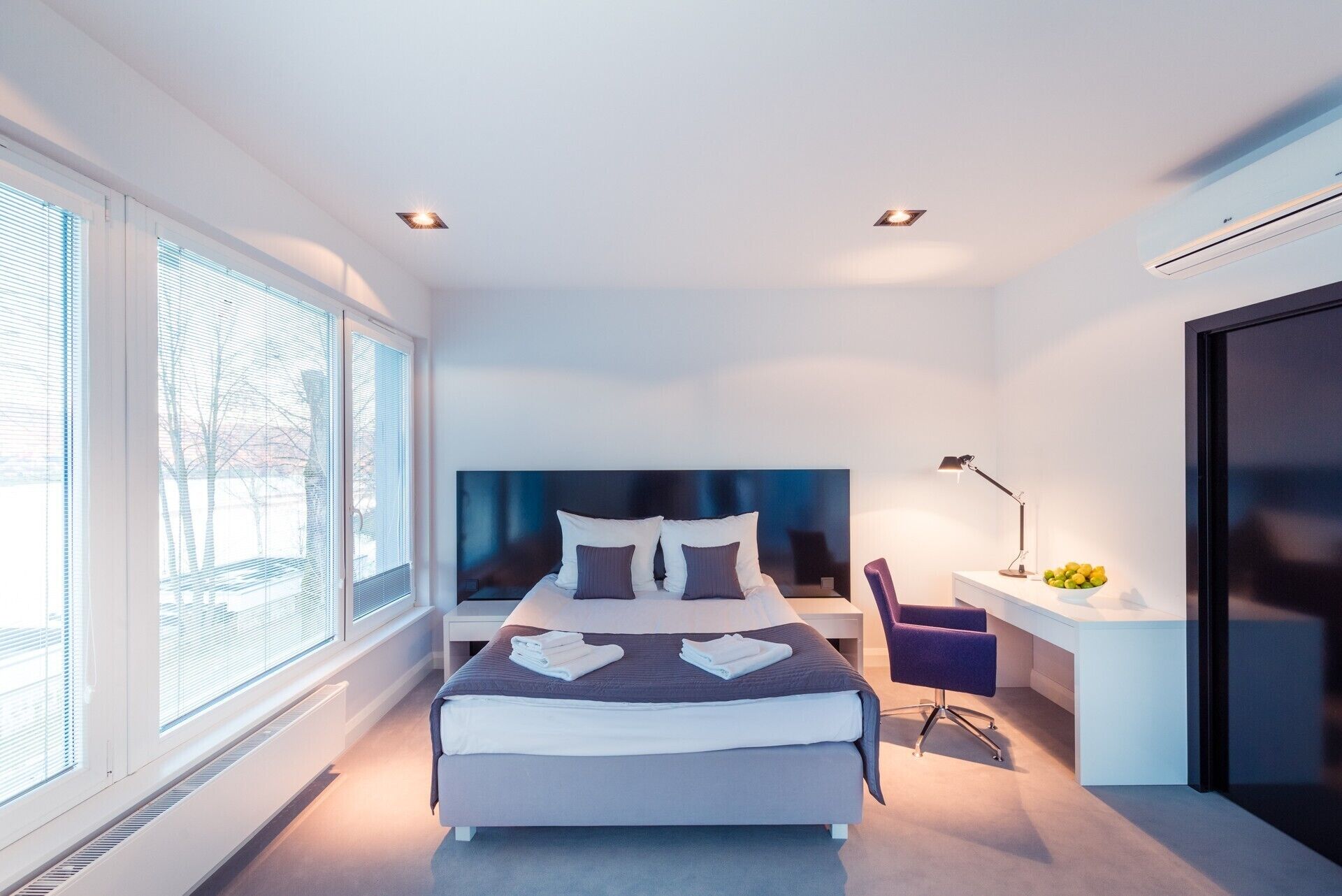 Un dormitorio moderno con una cama grande, un escritorio con silla y una ventana con persianas.