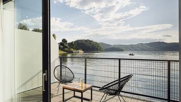Un balcone con un tavolo in legno e due sedie, affacciato su un fiume con barche e vegetazione sullo sfondo.