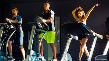 Tres personas usando cintas de correr en un gimnasio, con una puerta al fondo.
