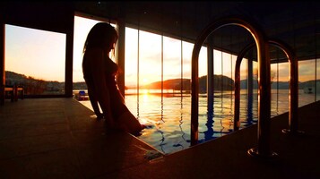 Uma pessoa perto de uma piscina, com vista para o pôr do sol sobre a água e colinas.