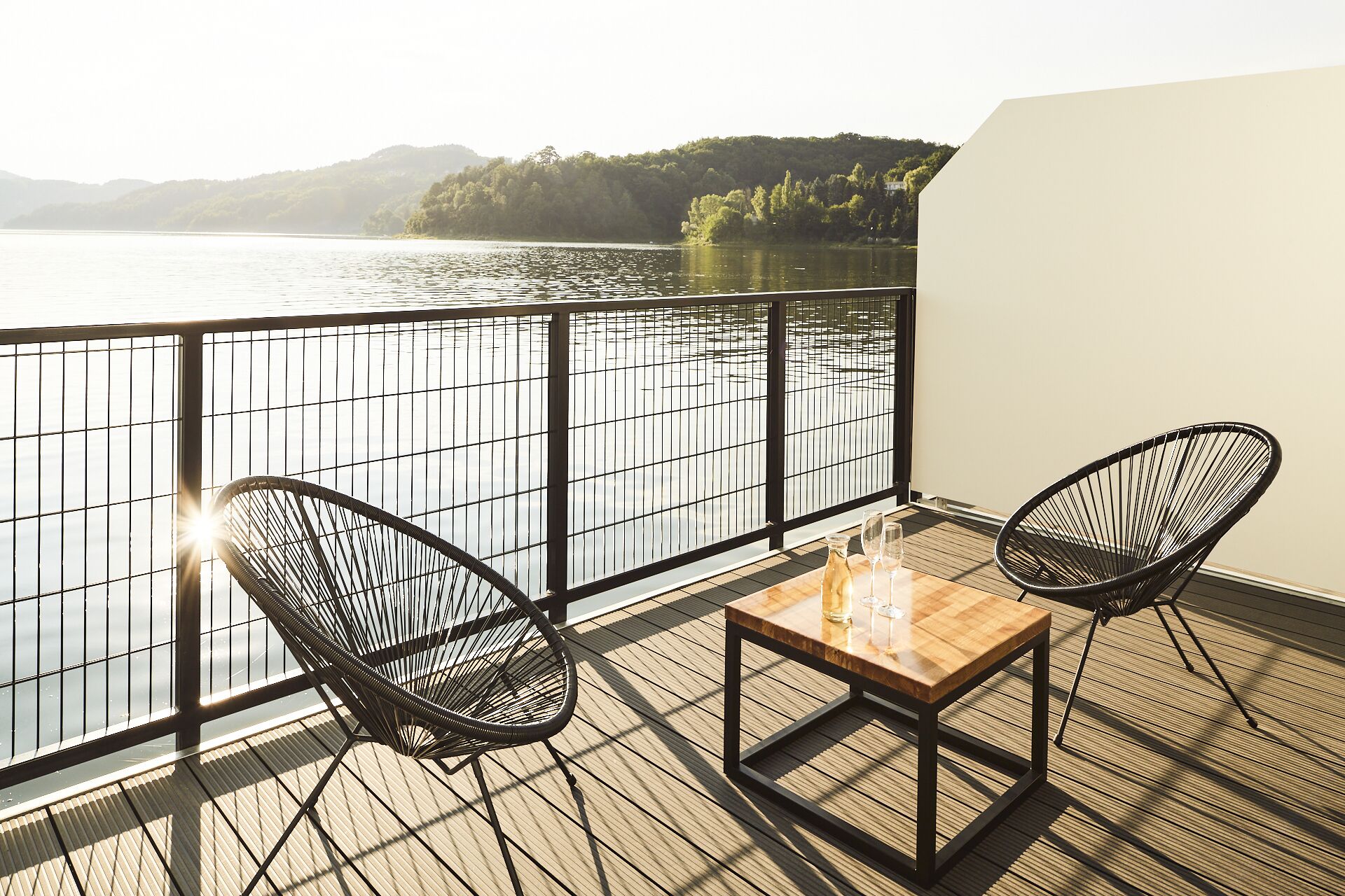 Terraza con dos sillas y una mesa con vista a un lago y colinas.
