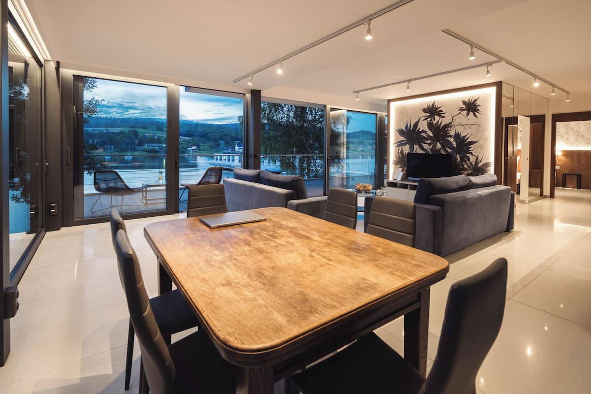 A modern interior with a dining area, sofas, and a large window offering a scenic view.