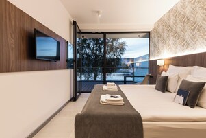 Quarto de hotel moderno com uma cama grande, televisão de tela plana na parede, varanda com vista para um lago e parede com padrão.