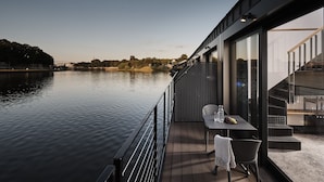 A modern outdoor deck with a table and chairs overlooking a calm body of water. - Lemon Resort Spa (Grodek Nad Dunajcem)