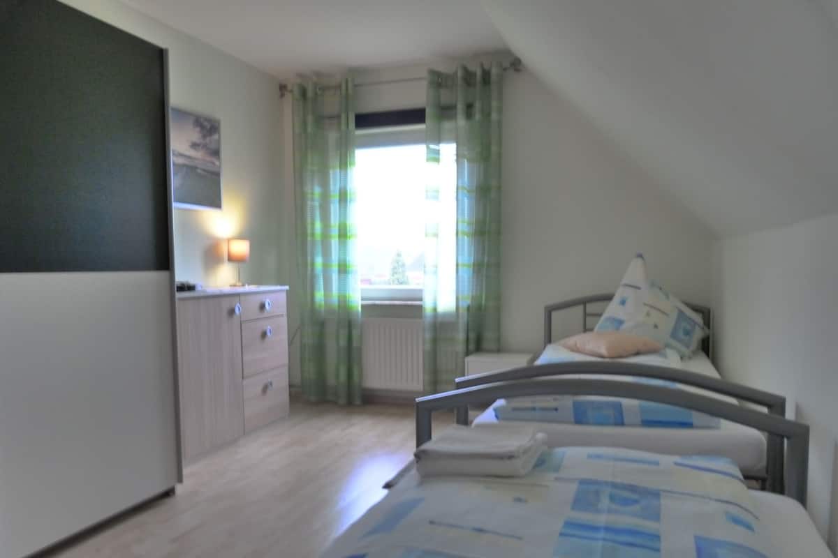 Un dormitorio con cama, cómoda, radiador y ventana con cortinas.