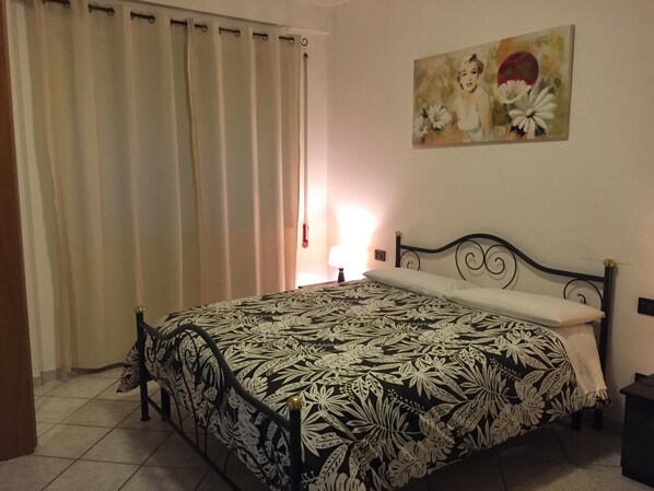A bedroom with a bed, curtains, a painting, and a bedside lamp. - M'ami Bed and Breakfast (Magliano de' Marsi)