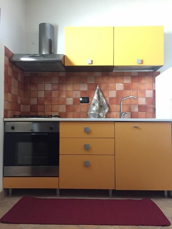 Una cocina con estufa, horno, armarios amarillos y una alfombra roja.