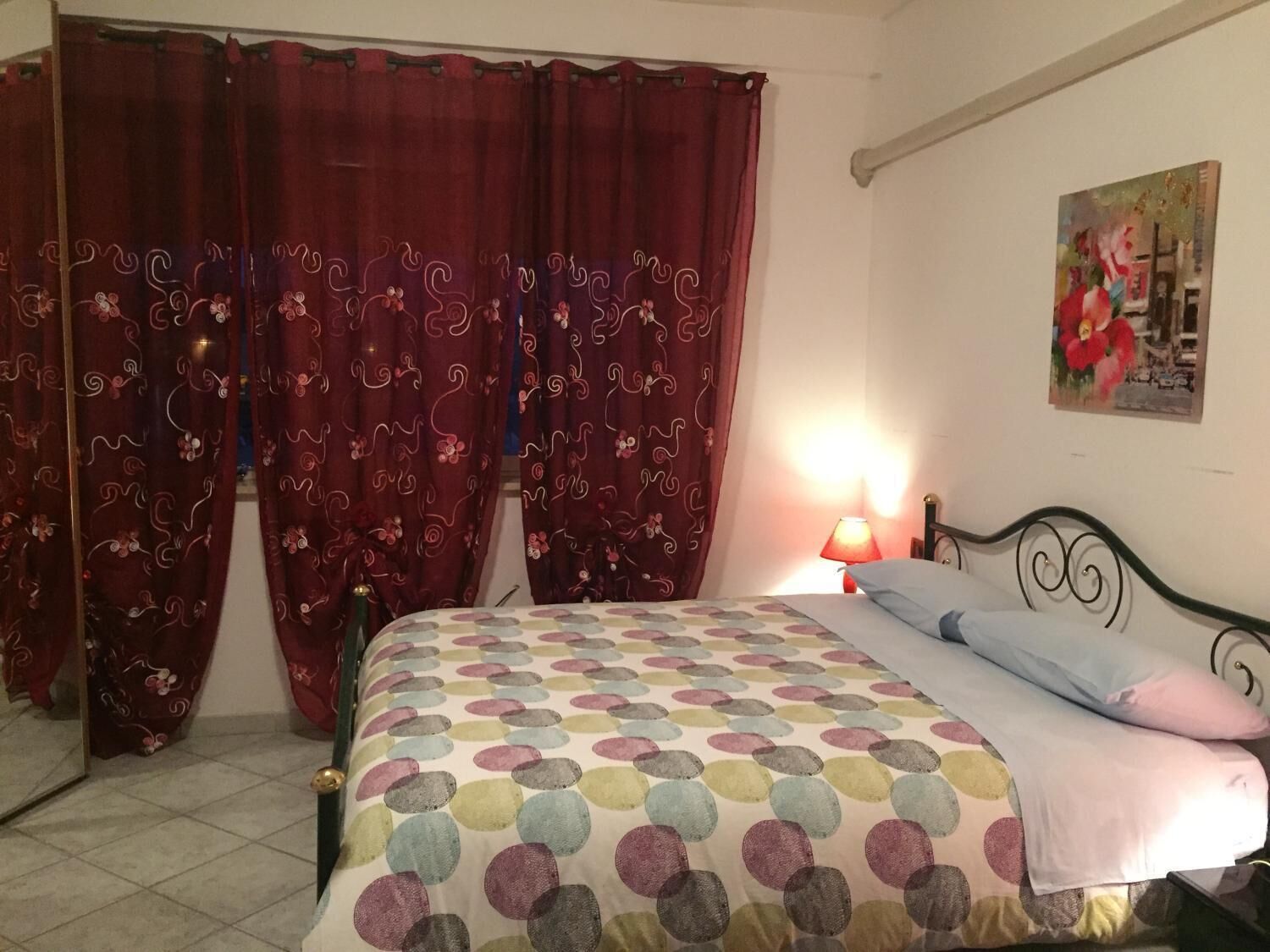 A bedroom with a bed, curtains, a lamp, and a painting on the wall.