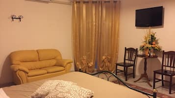 A hotel room with a bed, a sofa, a TV, and a small table with a vase of flowers.