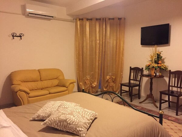 Habitación de hotel con cama, sofá, televisor y una pequeña mesa con un florero.