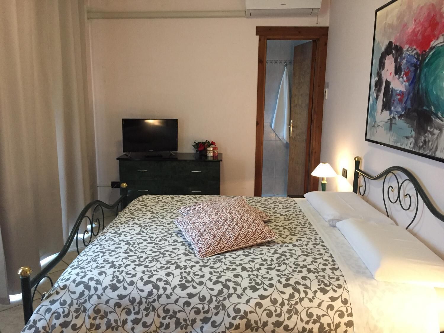 A bedroom with a bed, a dresser, a TV, and a painting on the wall.