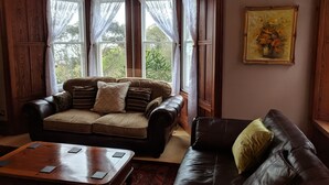 Un salon chaleureux avec un canapé en cuir marron, une table basse en bois et une fenêtre ornée de rideaux en dentelle.