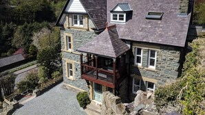 Une maison en pierre dotée d’un balcon, d’une cheminée et offrant une vue sur la forêt environnante.