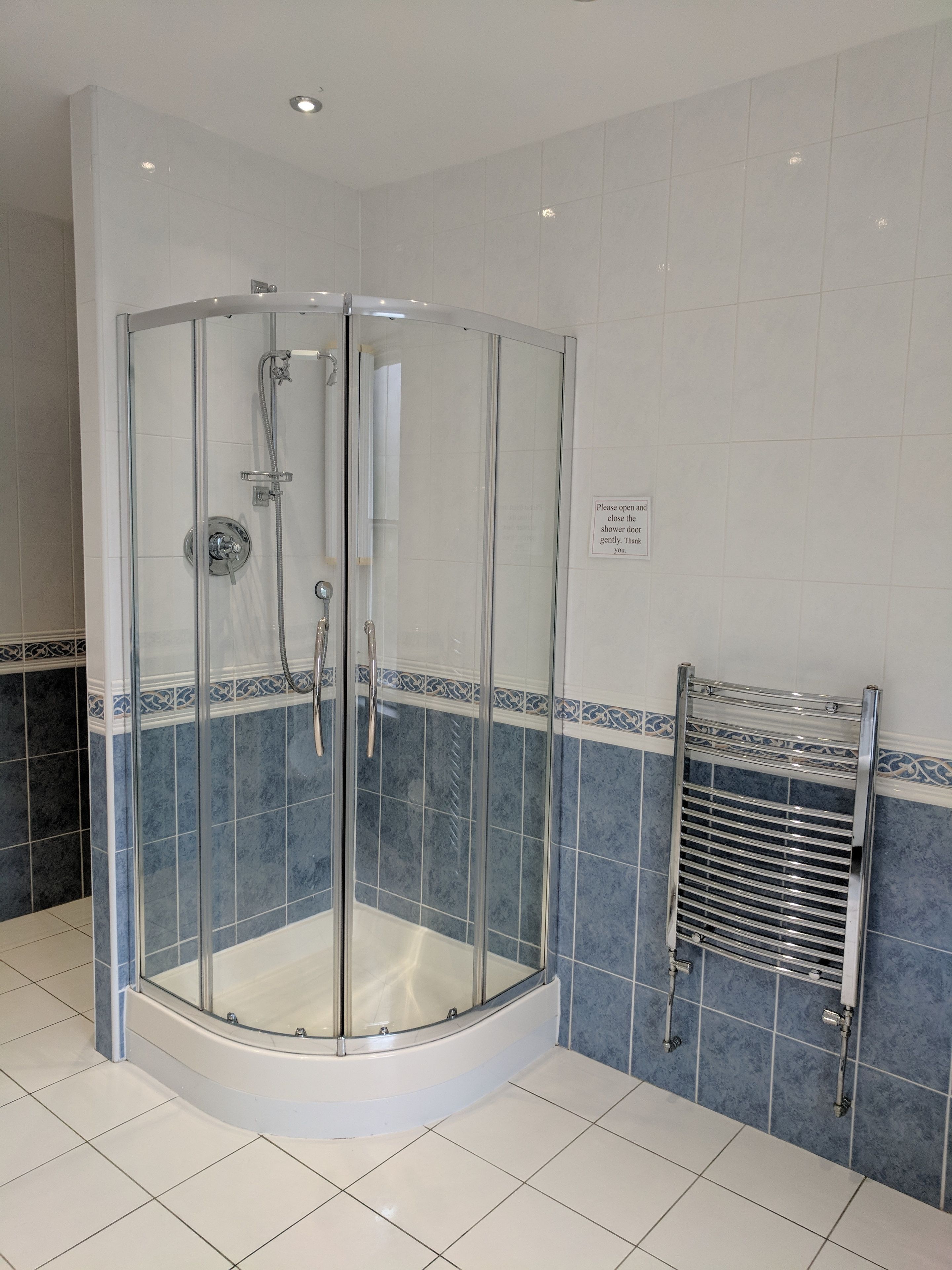 A glass-enclosed shower stall with a curved design, a towel rack, and a sign instructing to close the shower door gently.