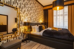 A modern hotel room with a geometric patterned wall, a large bed with multiple pillows, a bedside table with a lamp, and a large window with curtains. - Golden Prague Rooms (Prague)