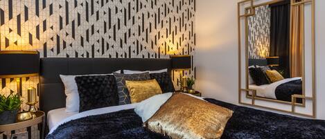 A modern bedroom with a geometric patterned wall, a large bed with multiple pillows, bedside lamps, and a mirror.