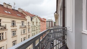 Vista de uma varanda com vista para uma rua com edifícios altos, grade de metal e carros estacionados.