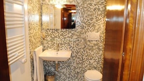 Un baño con pared de mosaicos, lavabo, inodoro y espejo.