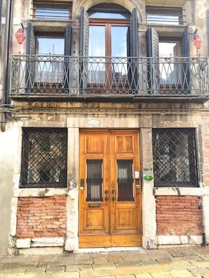 A two-story building with a wooden door, a balcony with metal railings, and windows with metal bars. - B&B San Firmino (Venice)