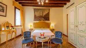 Una habitación con cama, dos sillas, una mesa con vasos, un espejo, un cuadro y un armario.