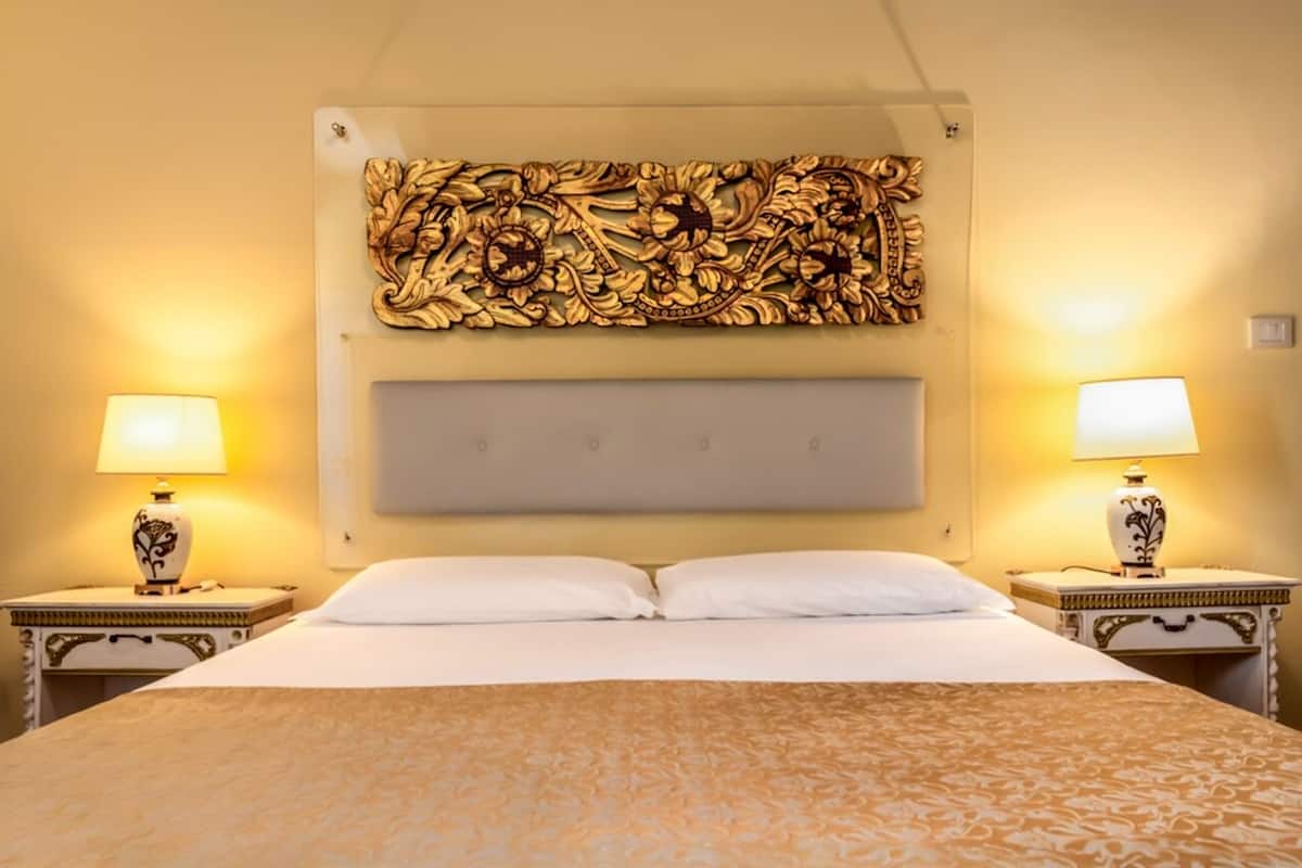 A hotel room with a large bed, two bedside tables with lamps, and a decorative wall piece above the bed.