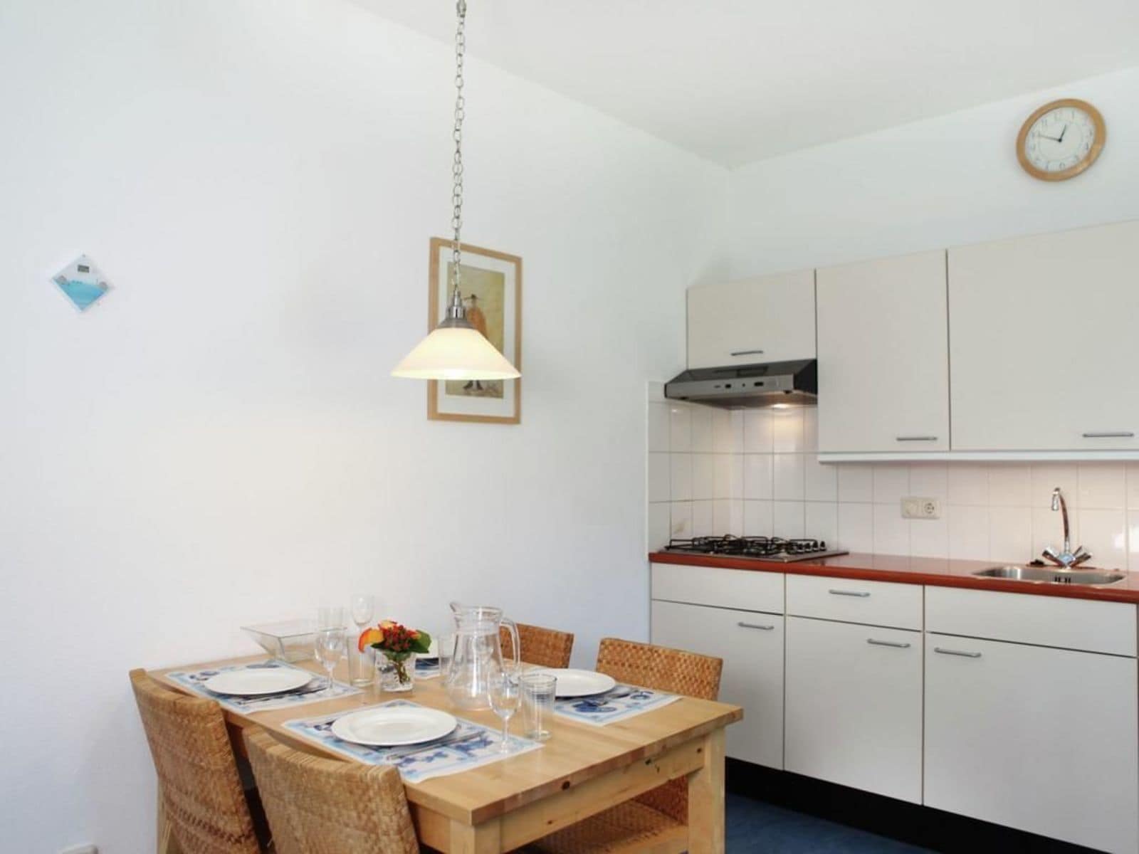 A compact kitchen with white cabinets, a gas stove, and a wooden dining table set for four.