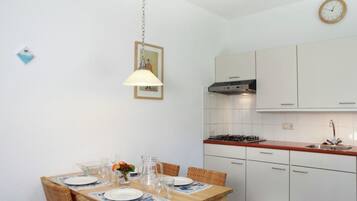 A compact kitchen with white cabinets, a gas stove, and a wooden dining table set for four.