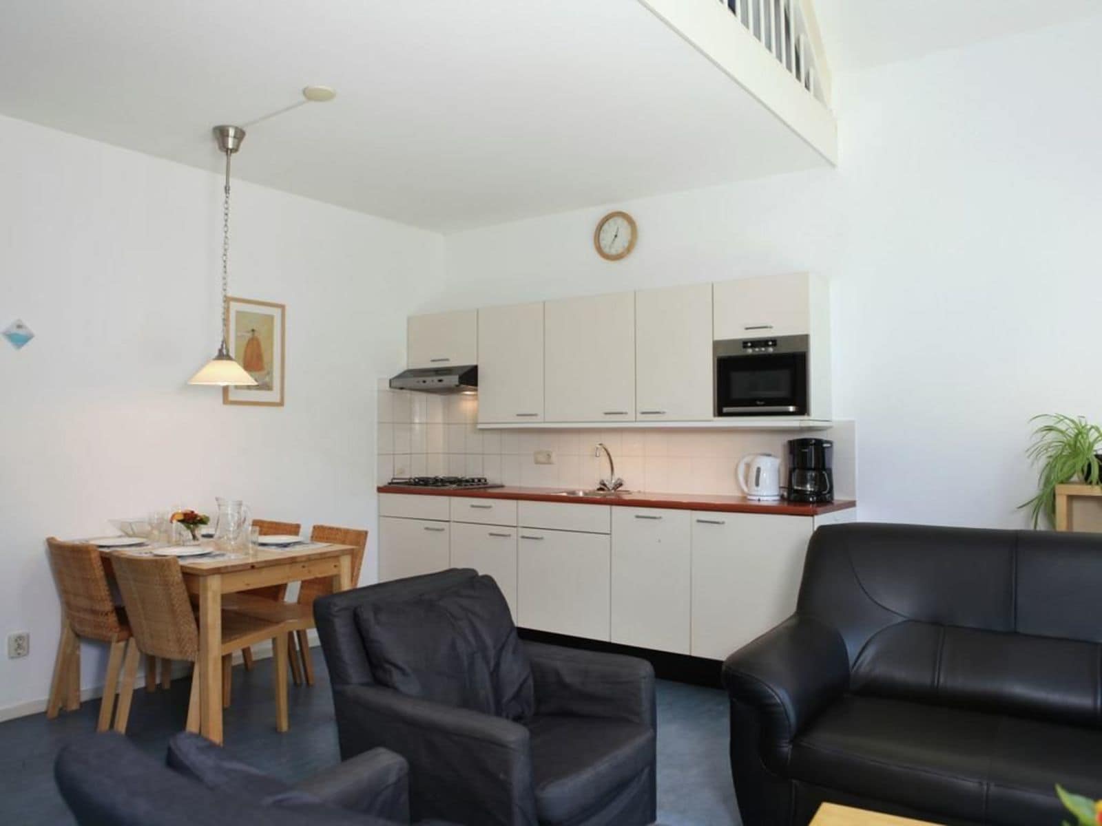 A compact living space with a dining area, a kitchenette, a black leather sofa, and a staircase.
