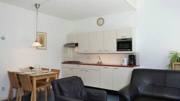 A compact living space with a dining area, a kitchenette, a black leather sofa, and a staircase.