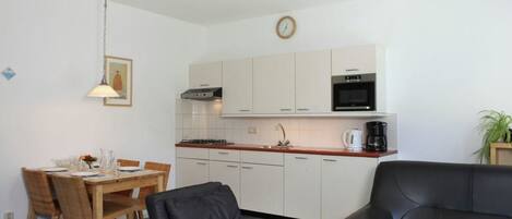 A compact living space with a dining area, a kitchenette, a black leather sofa, and a staircase.