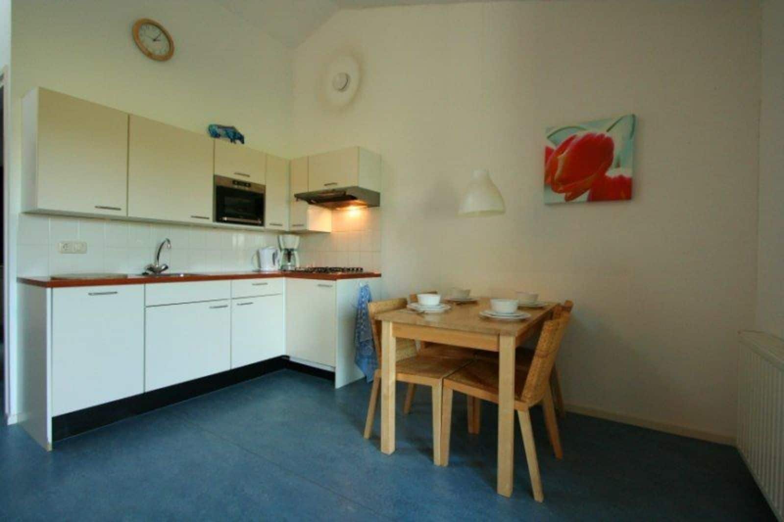 Een kleine keuken met witte kastjes, een houten eettafel en een blauwe vloer.