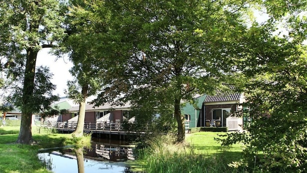 A riverside property with a small bridge, a grassy area, and a building with a sloped roof. - Rijnhoeve (Koudekerk aan den Rijn)