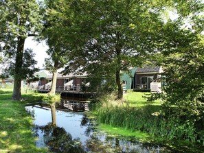 A riverside property with a small bridge, a grassy area, and a building with a sloped roof.