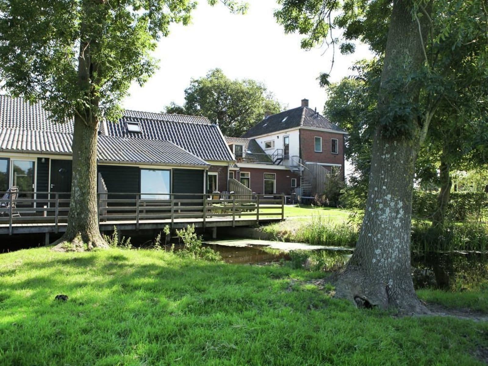 Ett traditionellt hus med en träveranda, en liten bro och en gräsig trädgård.