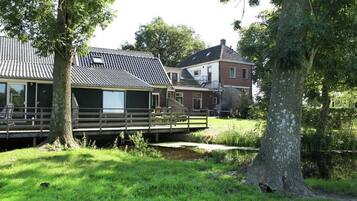 Ett traditionellt hus med en träveranda, en liten bro och en gräsig trädgård.