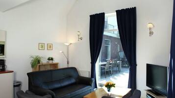 Una sala de estar con un sofá negro, dos sillones, una mesa de centro, un televisor y un ventanal con cortinas.