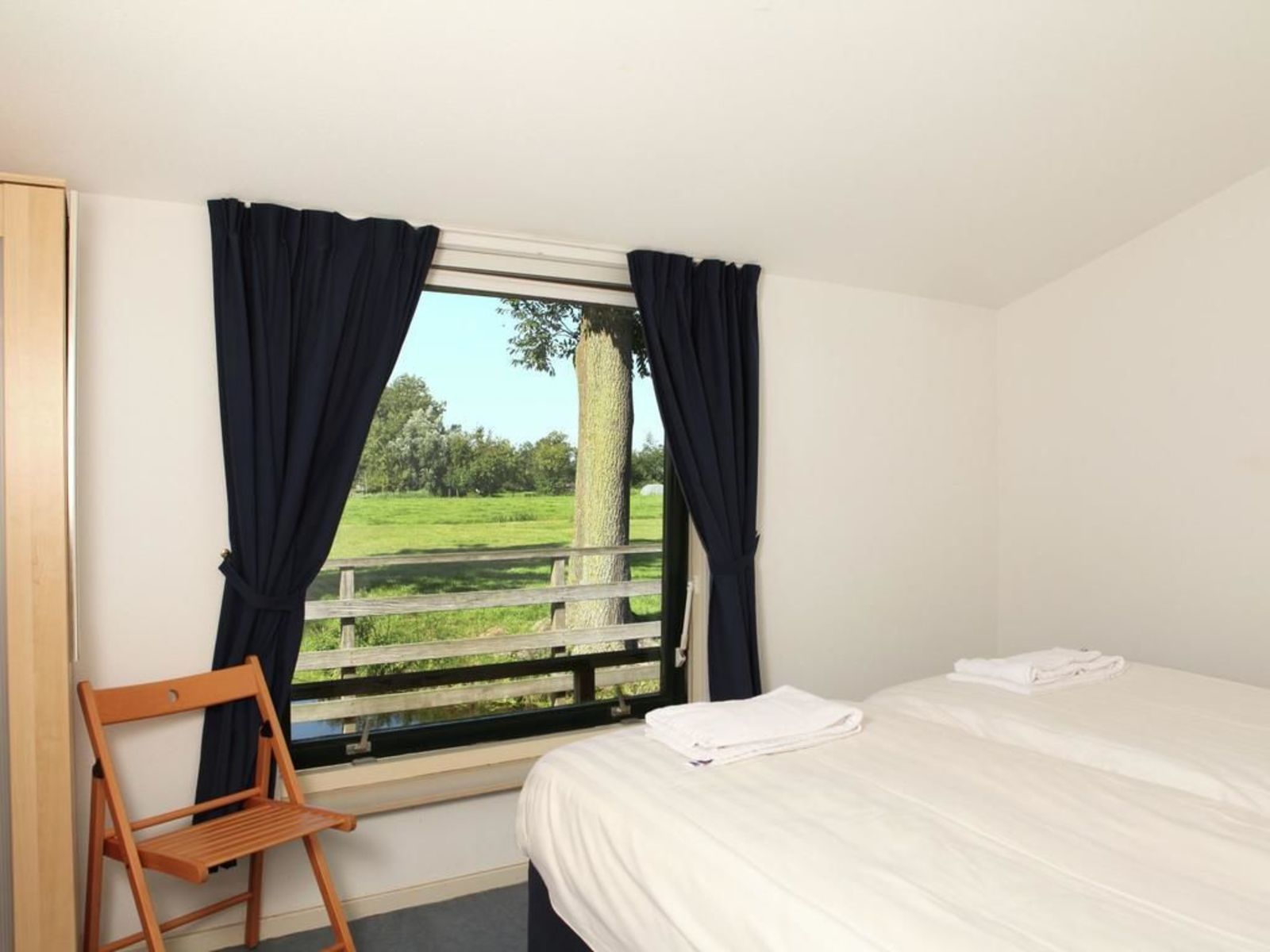 Un dormitorio con una cama, una silla de madera y una ventana con cortinas.