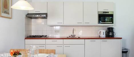 A modern kitchen with white cabinets, a wooden countertop, a gas stove, a sink, and a clock on the wall.
