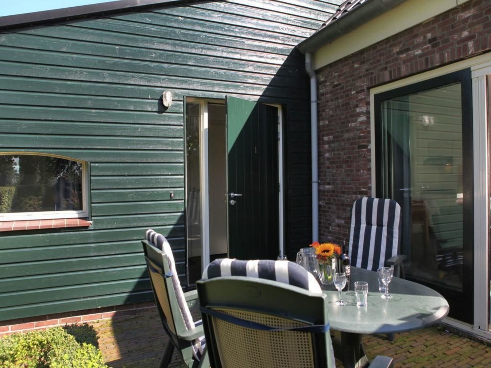 Un'area patio con tavolo e sedie, una porta scorrevole in vetro e una parete esterna verde.